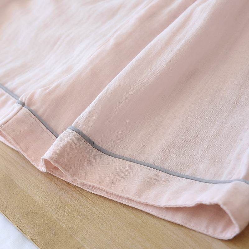 Close-up of light pink three-piece cotton gauze pajamas fabric with grey trim on wooden surface